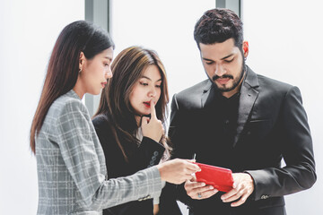 Closeup shot of two young millennial Asian doubtful female businesswomen in formal suit standing asking business solution ideas via tablet computer from Indian bearded male businessman manager mentor