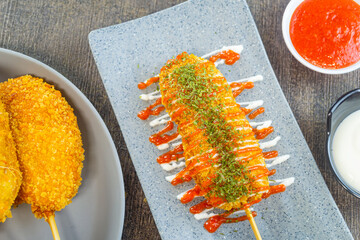 Mozarella Corndog served with mayonnaise, chili sauce and parsley. It has a savory taste and is cooked by frying