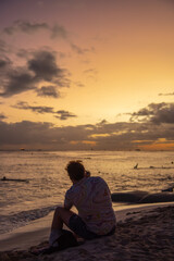 Persons silhouette sitting on the sand at a beautiful beach during sunset with orange, pastel sky background. 