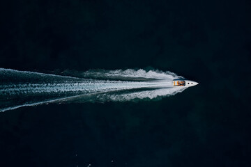 Super speed white boat fast movement on dark water top view. Fast moving white boat with people...