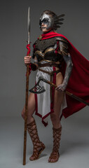 Studio shot of attractive woman warrior dressed in ancient armor holding axe and spear.