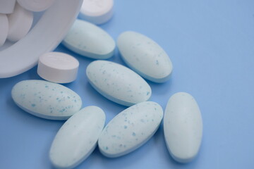 Pharmaceutical medical pills, blister-packaged capsules, and tablets strewn across a blue background.