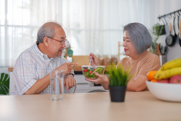 Fototapeta na wymiar Senior couple eating salad together at the kitchen at home. Concept of healthy nutrition in older age.