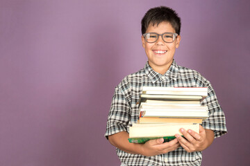 Happy smiling Latin student kid in eyeglasses holding books standing on purple background. Back to school concept. Copy space.