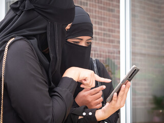 Two pretty Muslim women looking at smart phone checking message or looking at picture.