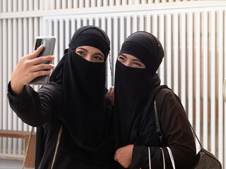 Lifestyle concept. Two pretty Muslim women taking selfie outdoors.