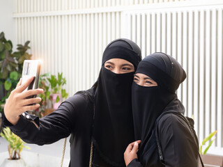 Two pretty Muslim women wearing black hijab or niqab taking selfie