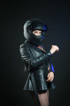 A young beautiful girl in a helmet and a black jacket poses in a dark studio.