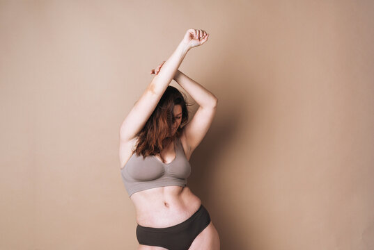 Young attractive woman plus size in underwear dancing on beige background, body love