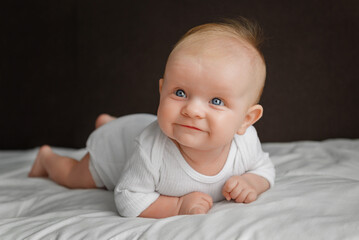 Cute baby lying on white bed sheet, close up view.