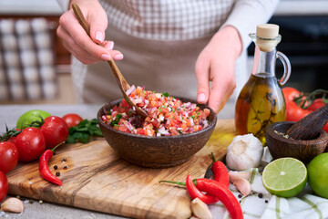 making salsa dip sauce - woman mixing chopped ingredients in wooden bowl