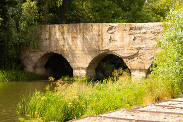 Fototapeta na wymiar Old abandoned stone bridge across the river in the Lipetsk region