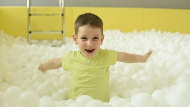 Cheerful child boy spending fun time in a dry pool with a lot of white plastic balls during his birthday