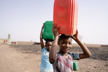 Close-up of two African girls carrying water canisters on their heads and walking towards the...