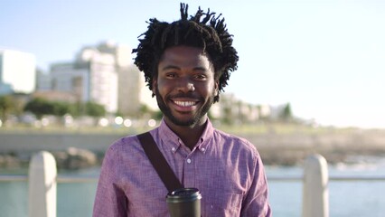 Portrait of trendy businessman taking daily commute, having coffee and enjoying view of the city against urban and ocean background. Smiling african american male with an edgy afro looking confident - Powered by Adobe
