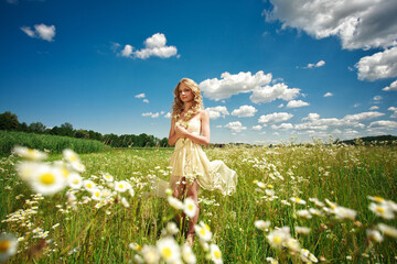 Beautiful girl on daisies field and  blue clouds sky background  in sunny summer day  outdoors portrait. young blonde  woman enjoys relaxing and have fun in nature on green grass  with white flowers