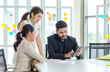 Two Asian young beautiful professional successful businesswoman employees presenting showing paperwork document on clipboard to Indian bearded male businessman manager to approve in meeting room