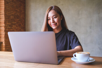 Portrait image of a young woman using and working on laptop computer with coffee cup on the table