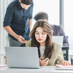 Closeup shot of millennial Asian young stressed depressed sleepy female businesswoman employee sitting holding hand on messy hair working on workstation desk via laptop notebook computer in office