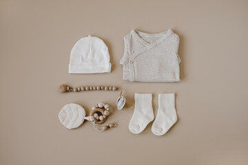 Basic bodysuit, hat, socks, pacifier with holder. Newborn baby clothes and accessories set on neutral pastel beige background. Fashion Scandinavian newborn clothes. Flat lay, top view.