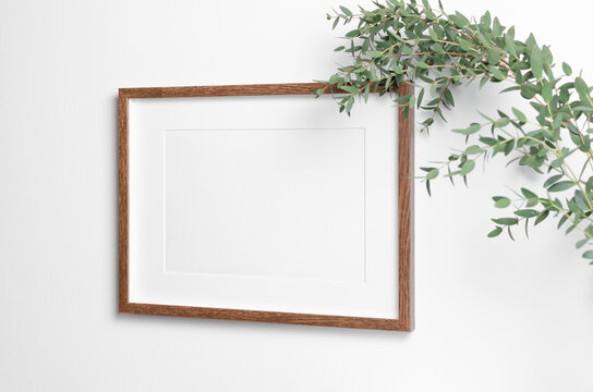 Frame mockup on white wall with fresh eucalyptus. Blank mockup copy space for art, painting or photo.