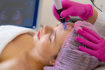 Beautician makes skin care procedure on a  face. Woman in a spa salon on cosmetic procedures for facial care. Cosmetologist making a woman a therapeutic laser processing on a face..