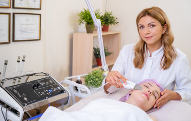 Woman in a spa salon on cosmetic procedures for facial care. Beautician makes medical procedures using a professional  equipment. Cosmetologist making a woman a therapeutic procedure on a face. .