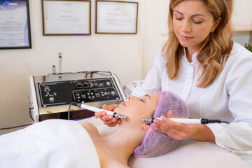 Cosmetologist making a woman a therapeutic procedure on a face.  Woman in a spa salon on cosmetic procedures for facial care. Beautician makes medical procedures using a professional  equipment...