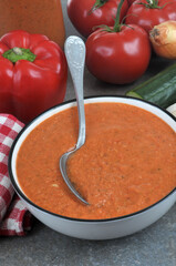 Assiette de gaspacho maison avec une cuillère et ses ingrédients en gros plan