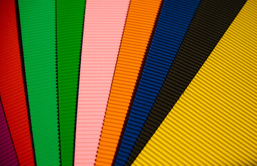 Abstract background made of corrugated paper for application. Space for text. Texture. Sheets of different colors lie in a fan. Green, red, blue, black, pink, orange color.