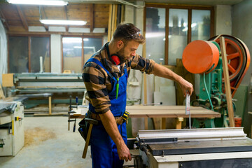 Bearded carpenter working on machine for straighten wood boards