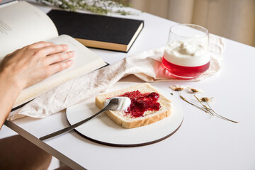 Break to eat. Pleasant and tasty moment of relaxation and tasting. Table with a glass of strawberry and yogurt gelatin and toast with red fruit jam. Selective focus.