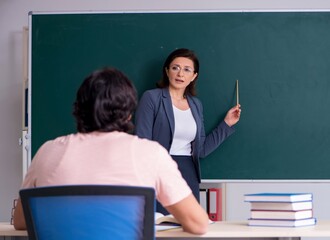 Old female teacher and male student in the classroom