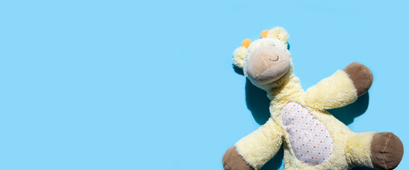 Children's soft toy giraffe on a blue background. Top view, flat lay. Banner