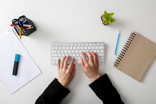 Female hands on the keyboard on a white table. Top view, flat lay