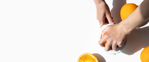 Woman's hand squeezes juice from an orange with a manual bowl on a white background. Top view, flat lay. Banner