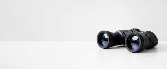 Black binoculars lying on a white background. Side view. Banner