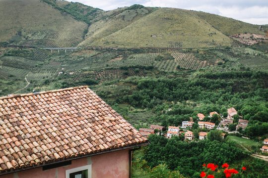 Top view of the Italian village of Nerola at the foot of a green hill with gardens. In the foreground is a house with old tiles, in the valley, there are Italian houses with red roofs.