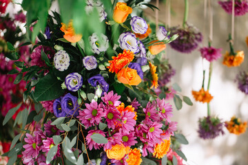 Bright Italian floral decor of multi-colored flowers, hanging flowers in the background. Pink chrysanthemums, gerberas, orange roses, Eustoma.