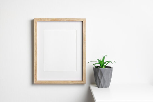 Portrait photo frame mockup on white wall with home plant in pot