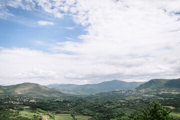 Green mountain landscape with blue cloudy sky. Orchards and small villages can be seen in the valley.