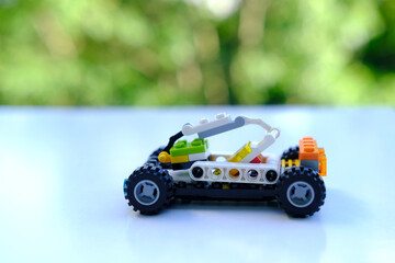 transformer car with manipulator, assembled from designer parts, beautiful green background of trees with bokeh, concept of development of fine motor skills, creativity, children's entertainment