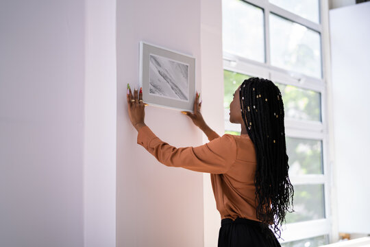 Woman Putting Photo Frame On Wall