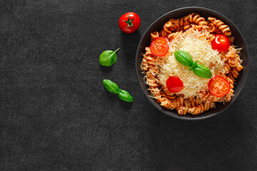Fusilli, cooked pasta with tomato sauce, basil, grated parmesan and cherry tomatoes, top view, space to copy text.
