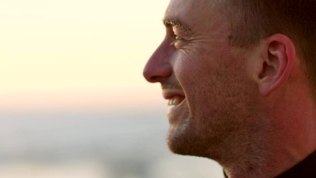 Closeup profile of a male face enjoying the sunset view standing outside against a blurred background. Happy smiling caucasian man at the beach at dawn relaxing on holiday with copy space