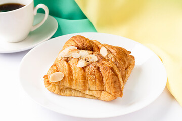 Almond croissant for breakfast on white plate with yellow green background, flat lay, top view.