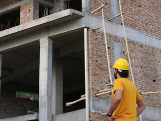 Young engineer wearing yellow safety helmet looking at blueprints in house at construction site