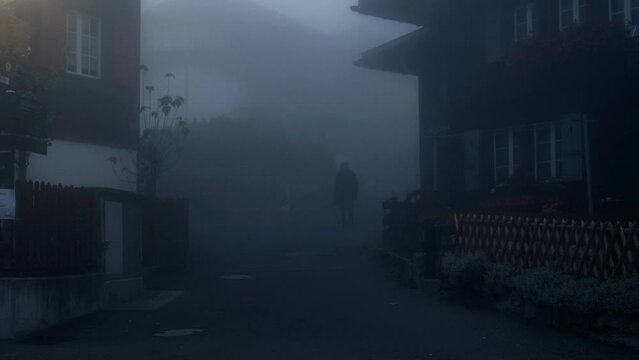 A man walks towards the camera in a mystic village covered with thick fog.