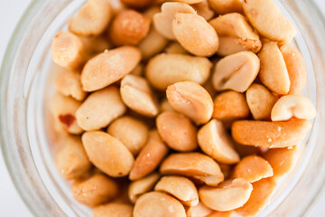 glass jar of peanuts on white marble background, healthy pantry ingredients