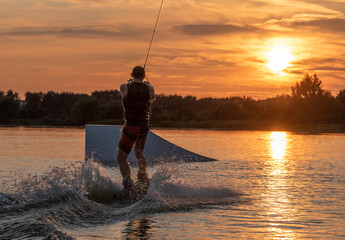 Wakeboarder making tricks. Low angle shot of man wakeboarding on a lake. Man water skiing at sunset.